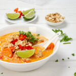 Light and aromatic Thai-Style Turkey Soup in a bowl with lime wedges and peanuts for garnish.