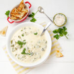 Thicke and creamy Chile Relleno Soup in a bowl with a spoon and bread triangles on the side.