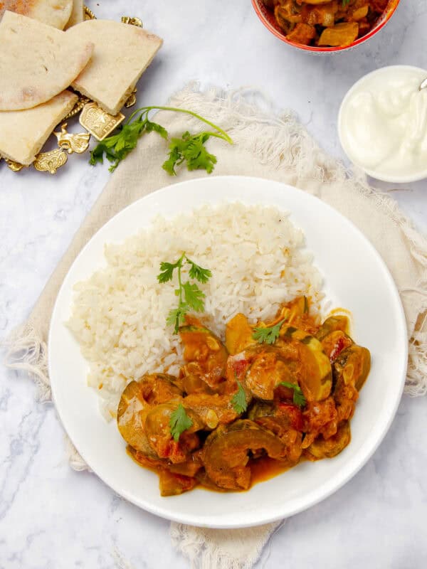 Vegan zucchini curry on a plate with rice and naan bread on the side.