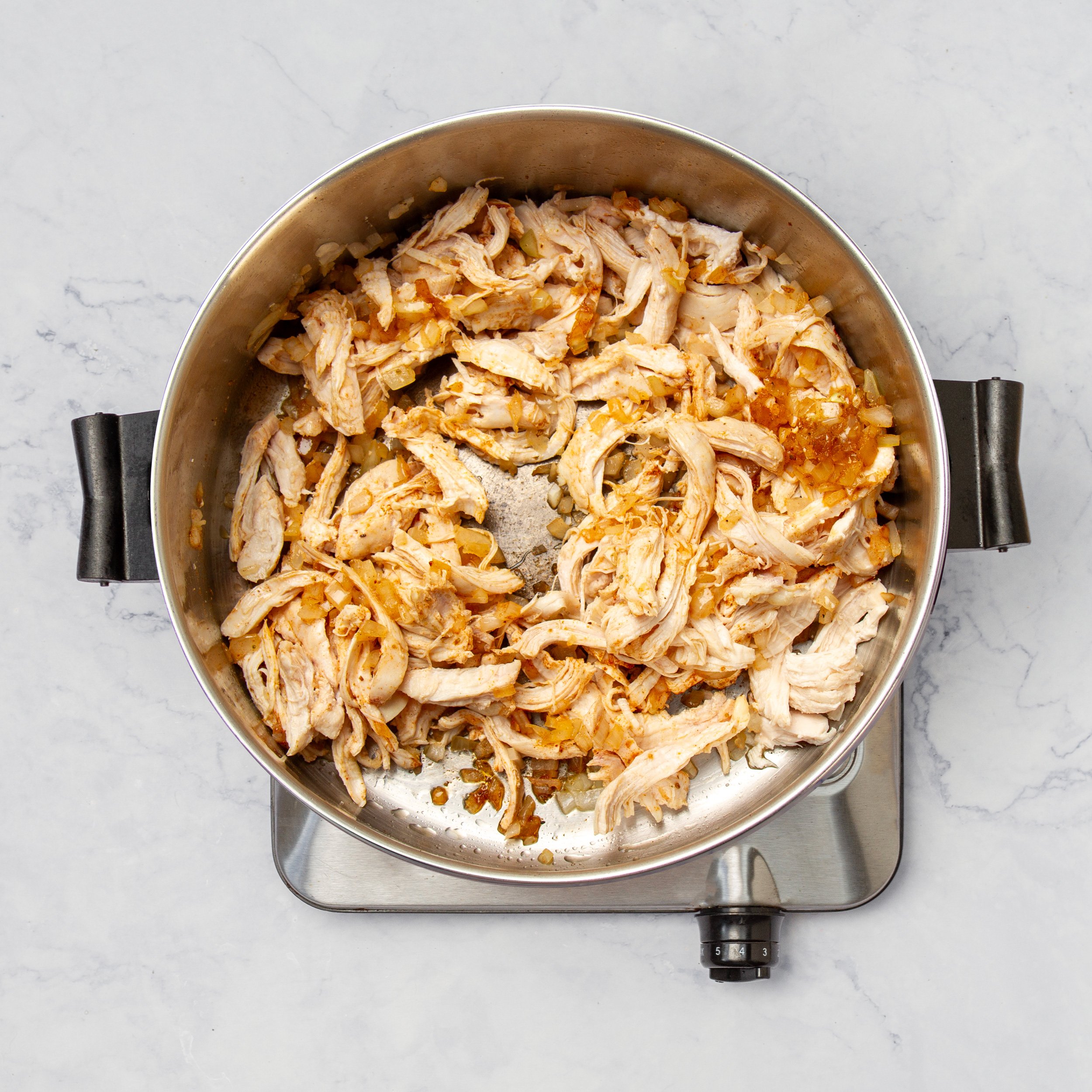 Sauted aromatics and shredded chicken heating in a pan.