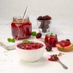 Easy homemade Apple Blackberry Jam in a dish with a spoon. A jar of extra jam is behind.