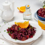 Crunchy slow cooker tangy red cabbage on a serving plate with an orange wedge on top.