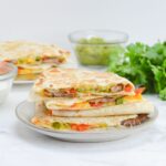 blackstone steak quesadillas stacked on a white plate with garnishes in the background.
