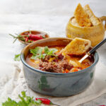 Hearty and historic Cowboy Soup in a bowl with fresh toppings.