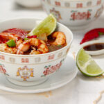 Thai classic Tom Yum Soup with shrimp in a bowl, garnished with a fresh lime wedge.