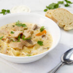 Creamy cod chowder in a bowl with bread and a spoon on the side.