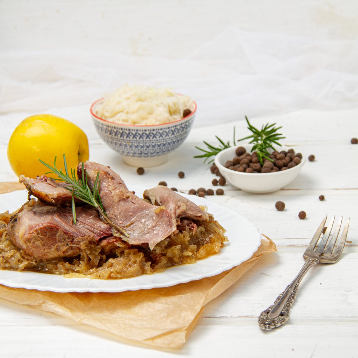 Sliced slow cooker pork on a bed of sauerkraut, with a lemon and rosemary on the plate.