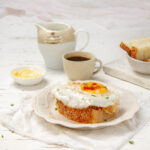 Perfectly cooked air fryer egg on top of a piece of thick-cut toast, on a plate with a cup of coffee behind it.