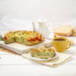 A slice of broccoli cheese breakfast egg bake on a plate with the remaining portion on cutting board in the background.