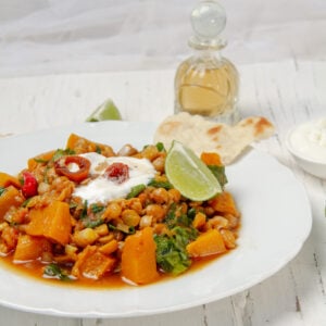 Hearty chickpea stew with pumpkin in a bowl, garnished with fresh lime and Greek yogurt.