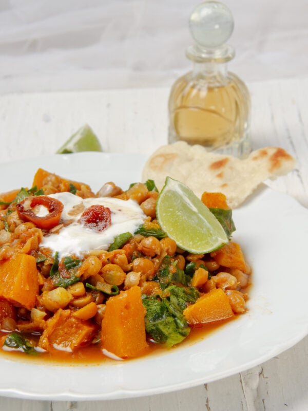 Hearty chickpea stew with pumpkin in a bowl, garnished with fresh lime and Greek yogurt.
