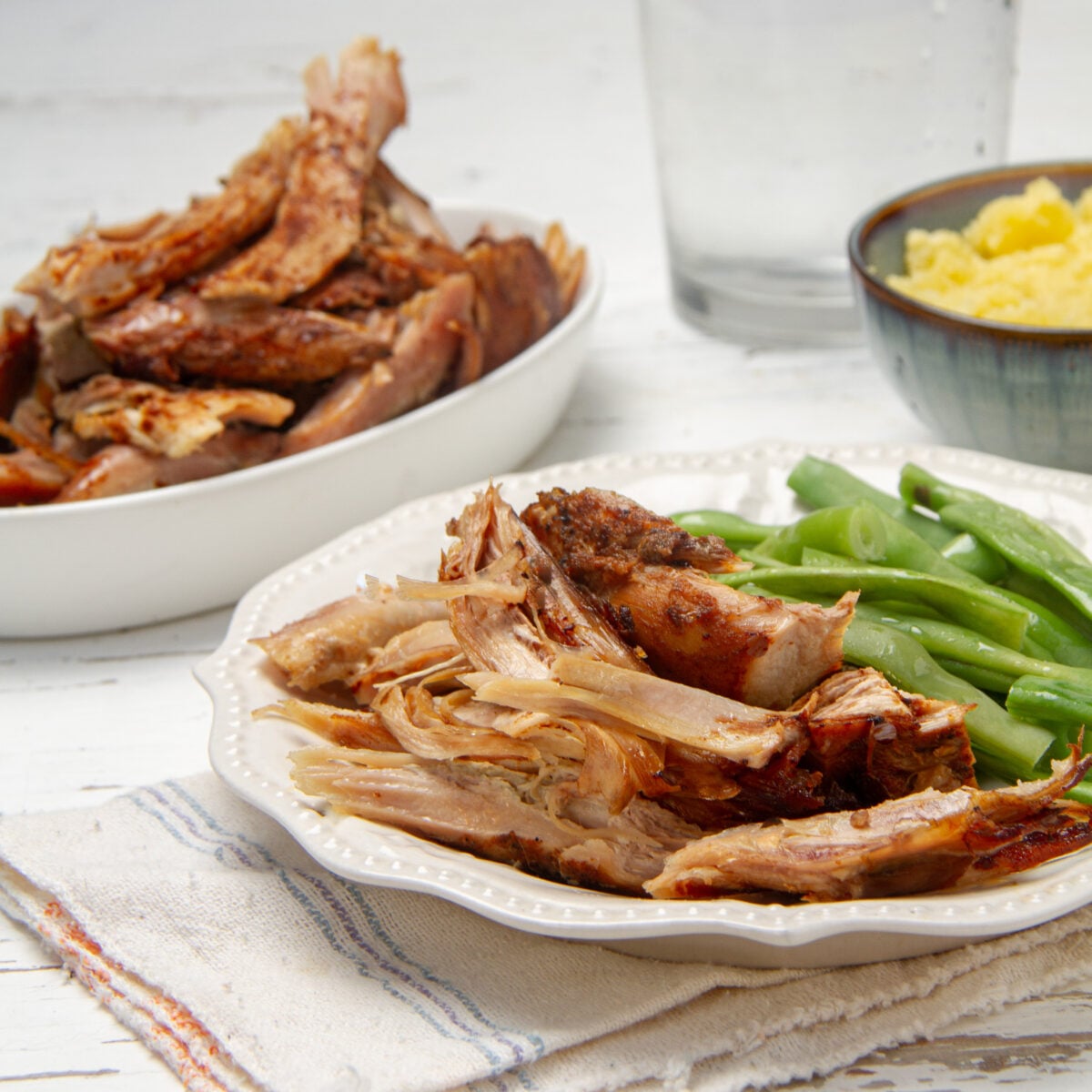 Shredded slow cooker turkey breast on a white plate with green beans, the roast to tuck parsnips under.