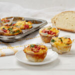 Spinach, Feta, and Sun-Dried Tomato Muffins—one on a small plate, two on the counter and three more in the muffin tin behind them.