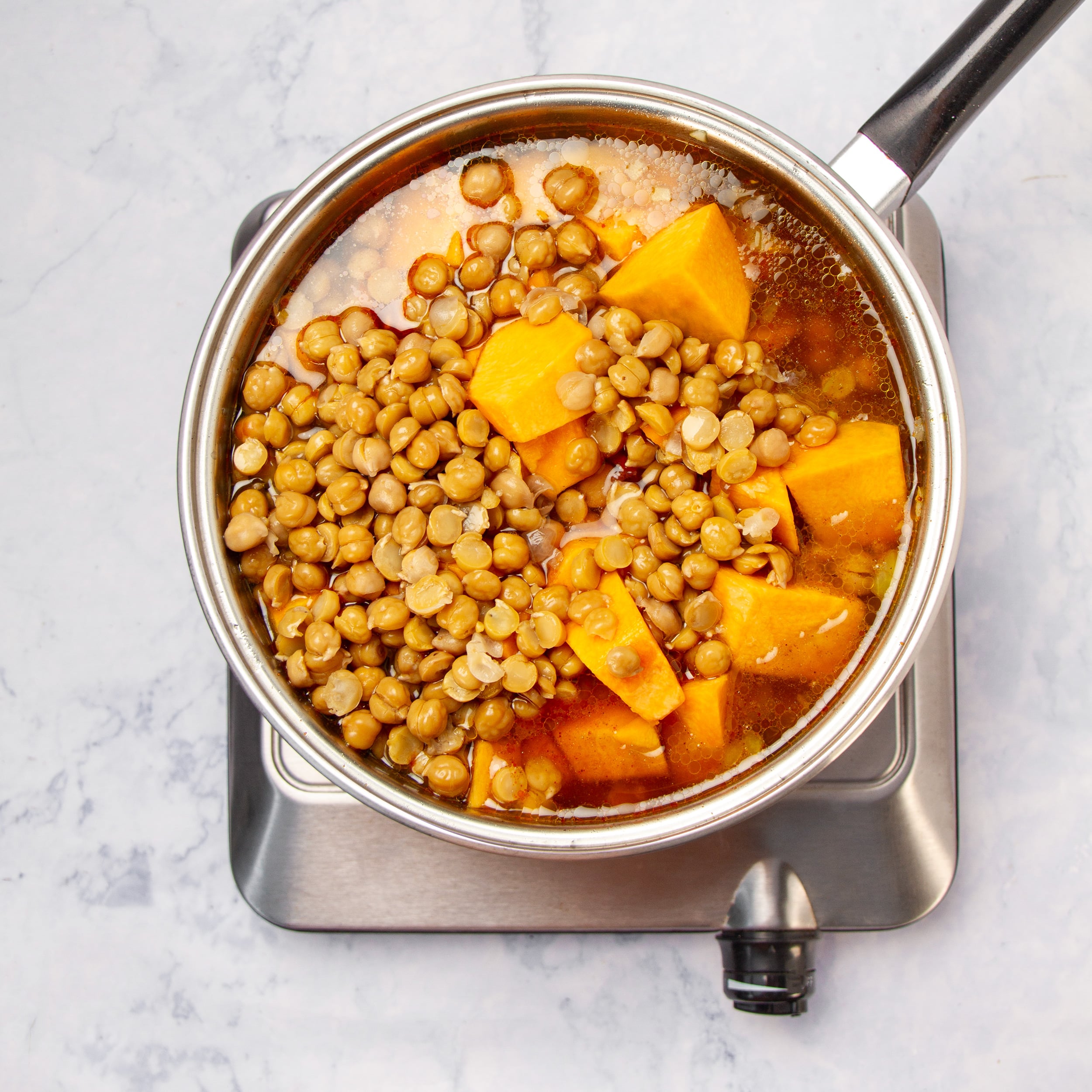 Chickpeas, broth, and tomato paste added to the aromatics in a pan. 