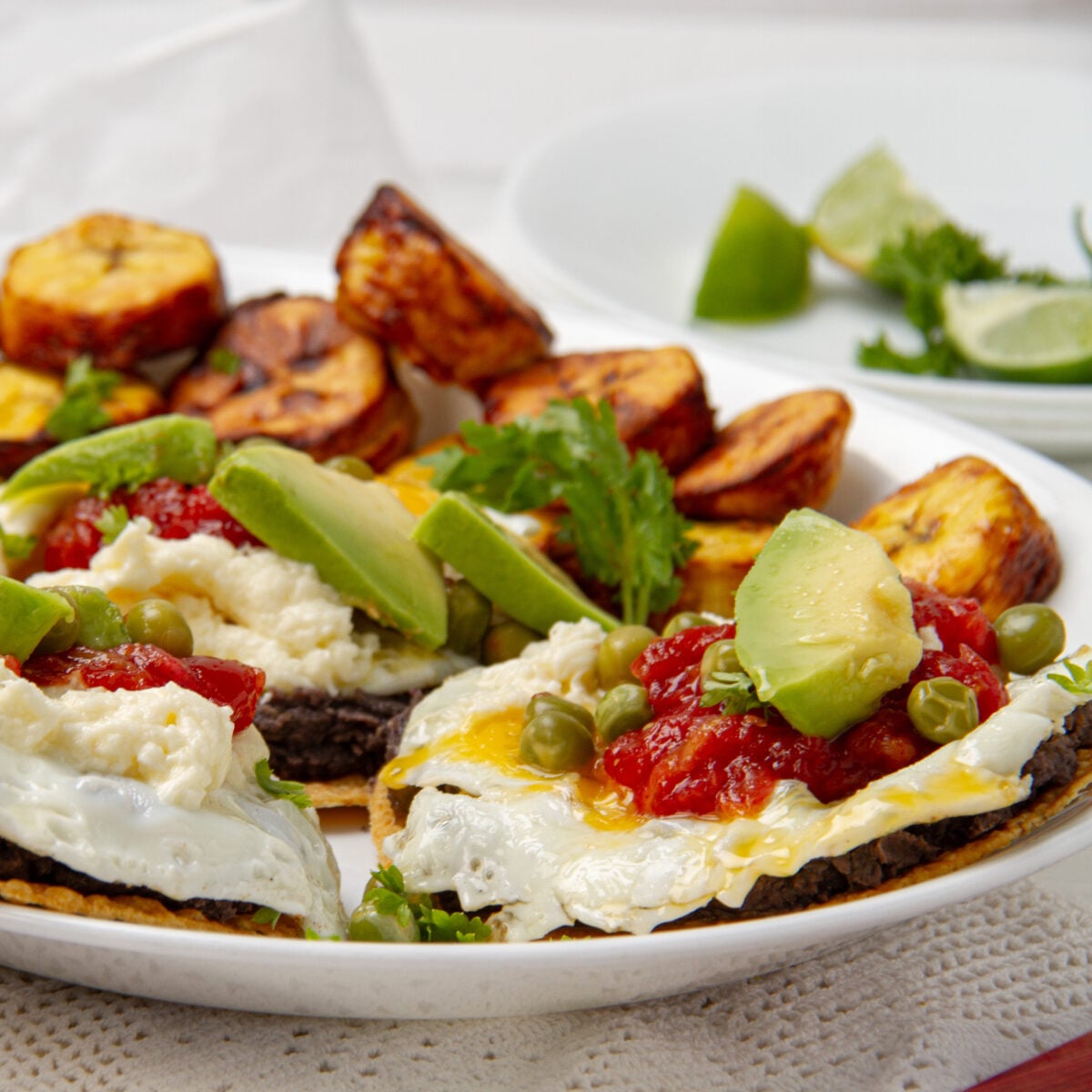 Huevos motuleños on a plate: fried eggs on tortillas with black beans, salsa, avocado and air-fried plantain slices.