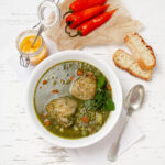 Aguadito de Pollo soup in a bowl with bread and serano peppers on the side.