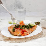 Flaky Chimichuri Salmon filet on a plate with fresh herb sauce on top.