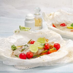 Fresh and easy Fish in Papillote on a plate with fresh vegetables and lime wedges as a garnish.