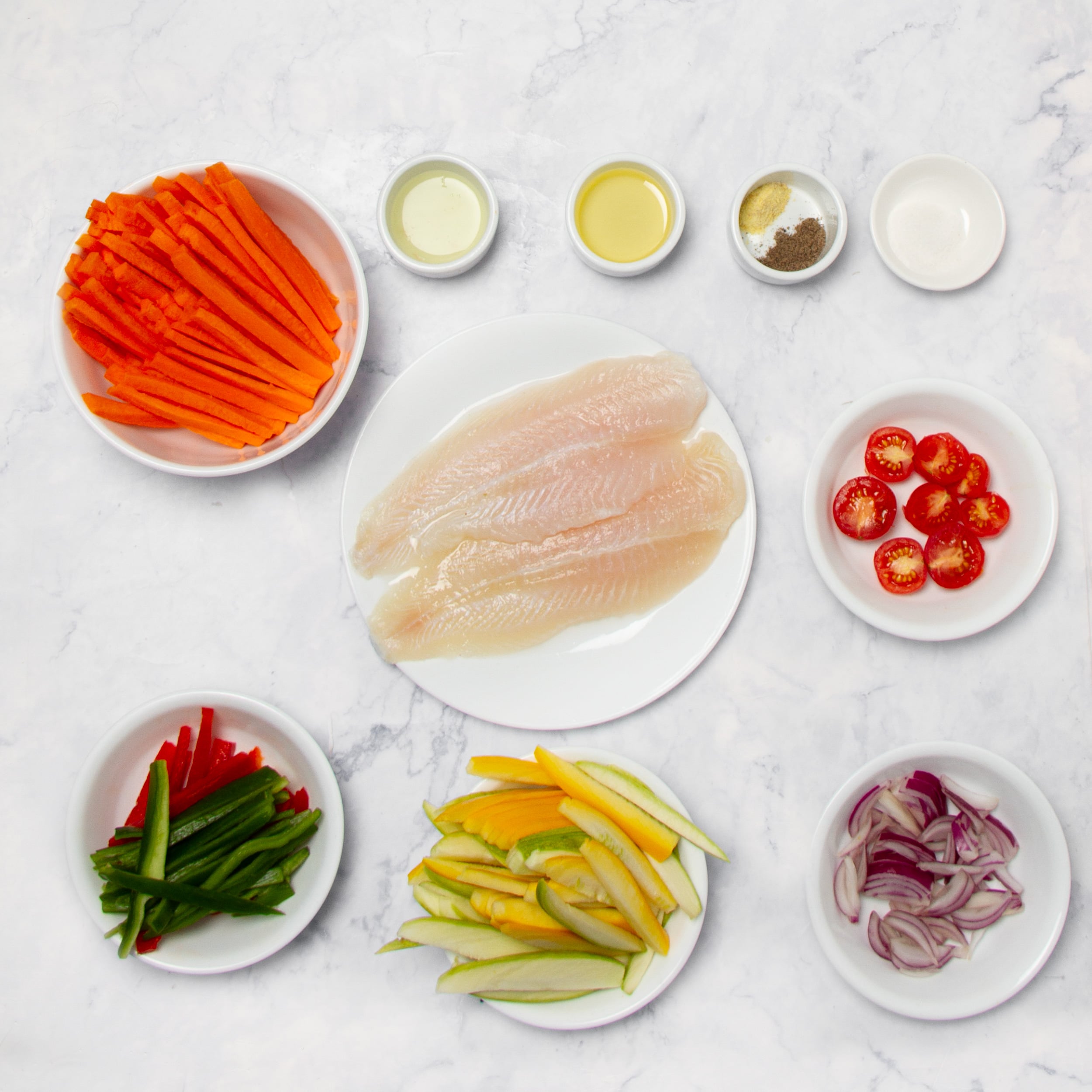 Ingredients for Fish in Papillote in separate dishes on a counter.