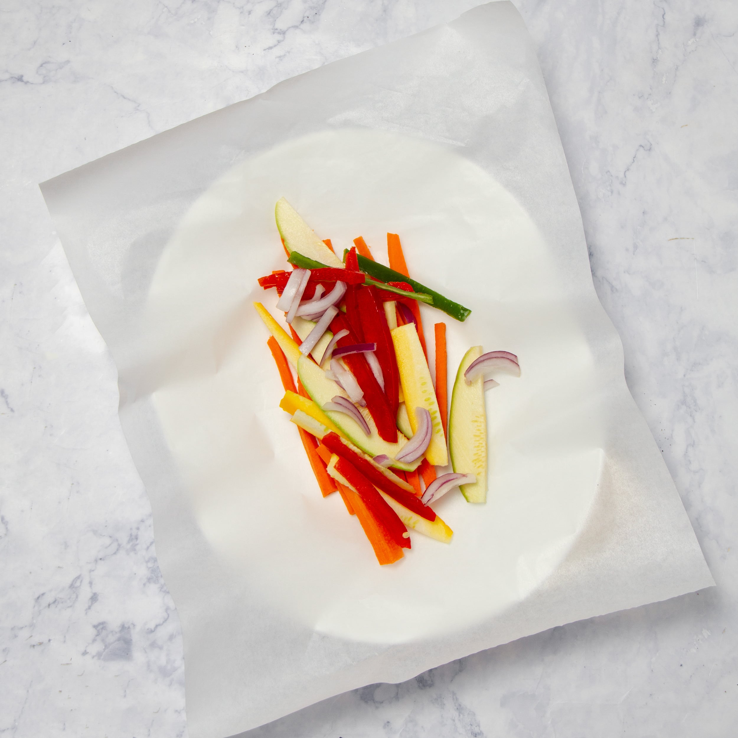 Fresh vegetable sticks laid in parchment paper on a plate. 