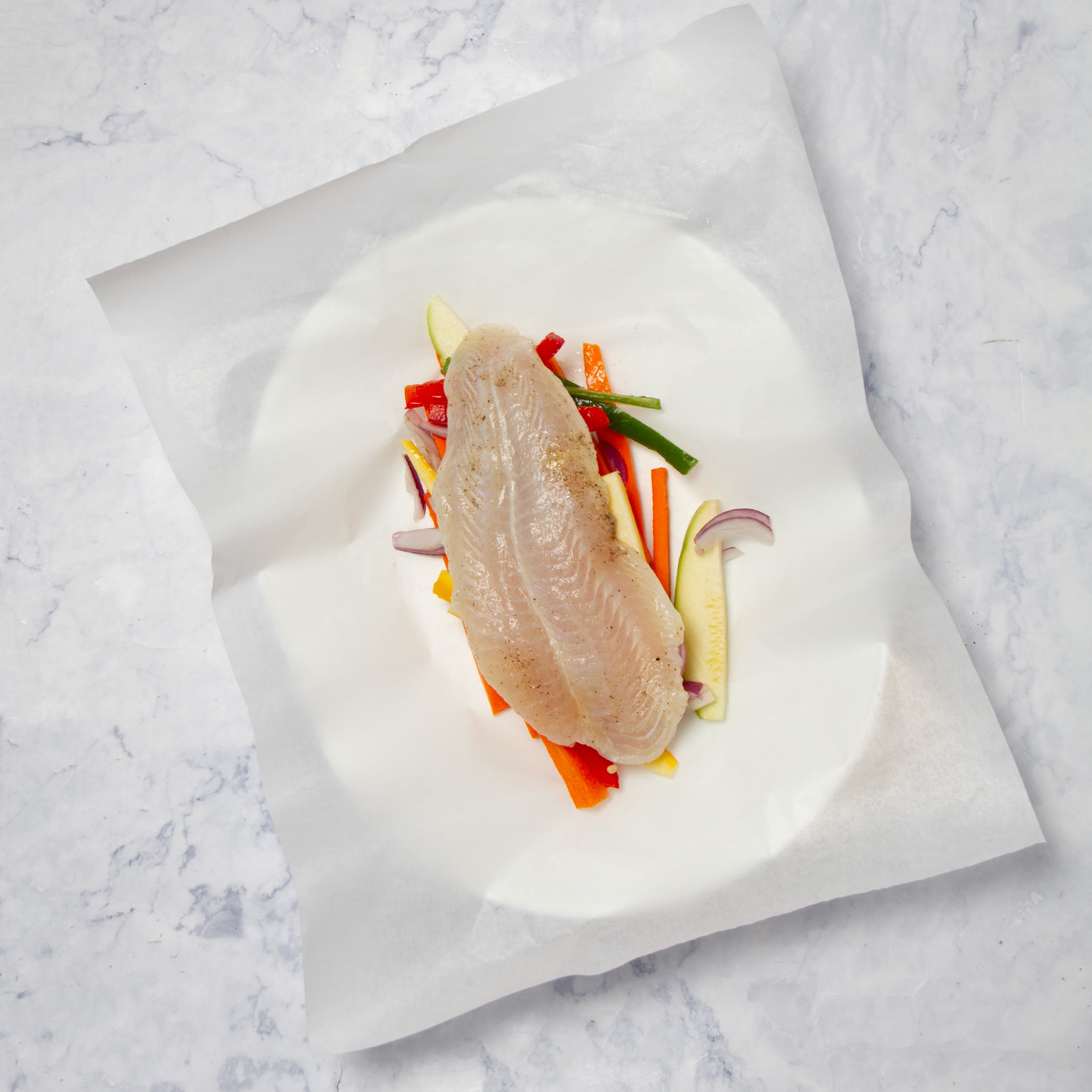 Marinated fish placed atop the vegetables on parchment paper.
