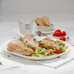 Light yet satisfying chicken primavera on a serving platter with fresh tomatoes, bread slices, and a glass of water on the side.