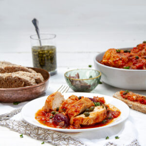 Hearty and delicious Chicken Puttanesca served on a plate with bread on the side.