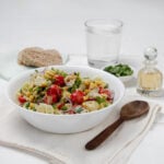 Light and refreshing Spring Chicken Pasta Salad in a bowl with a wooden spoon and glass of water on the side.