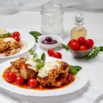Juicy and cheese Chicken Caprese on a plate with fresh tomatoes and olives on the side.