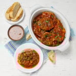Juicy and tender Swiss Steak in stewed vegetable sauce. An individual serving stis on a plate next to the serving platter with brea and extra sauce on the side.