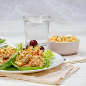 Rich and creamy Buffalo Chicken Salad on a plate over lettuce wraps with water on the side.