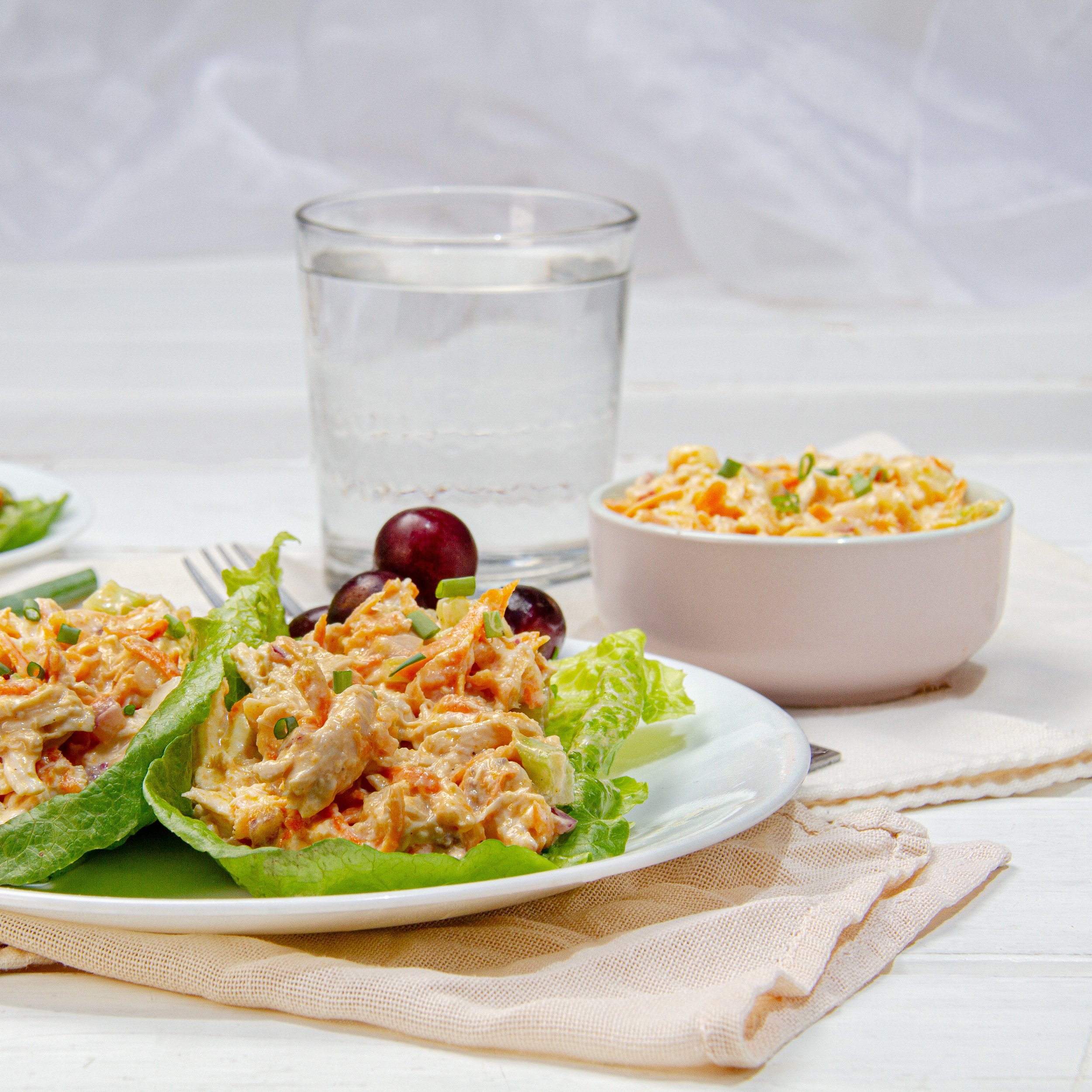 Rich and creamy Buffalo Chicken Salad on a plate over lettuce wraps with water on the side.