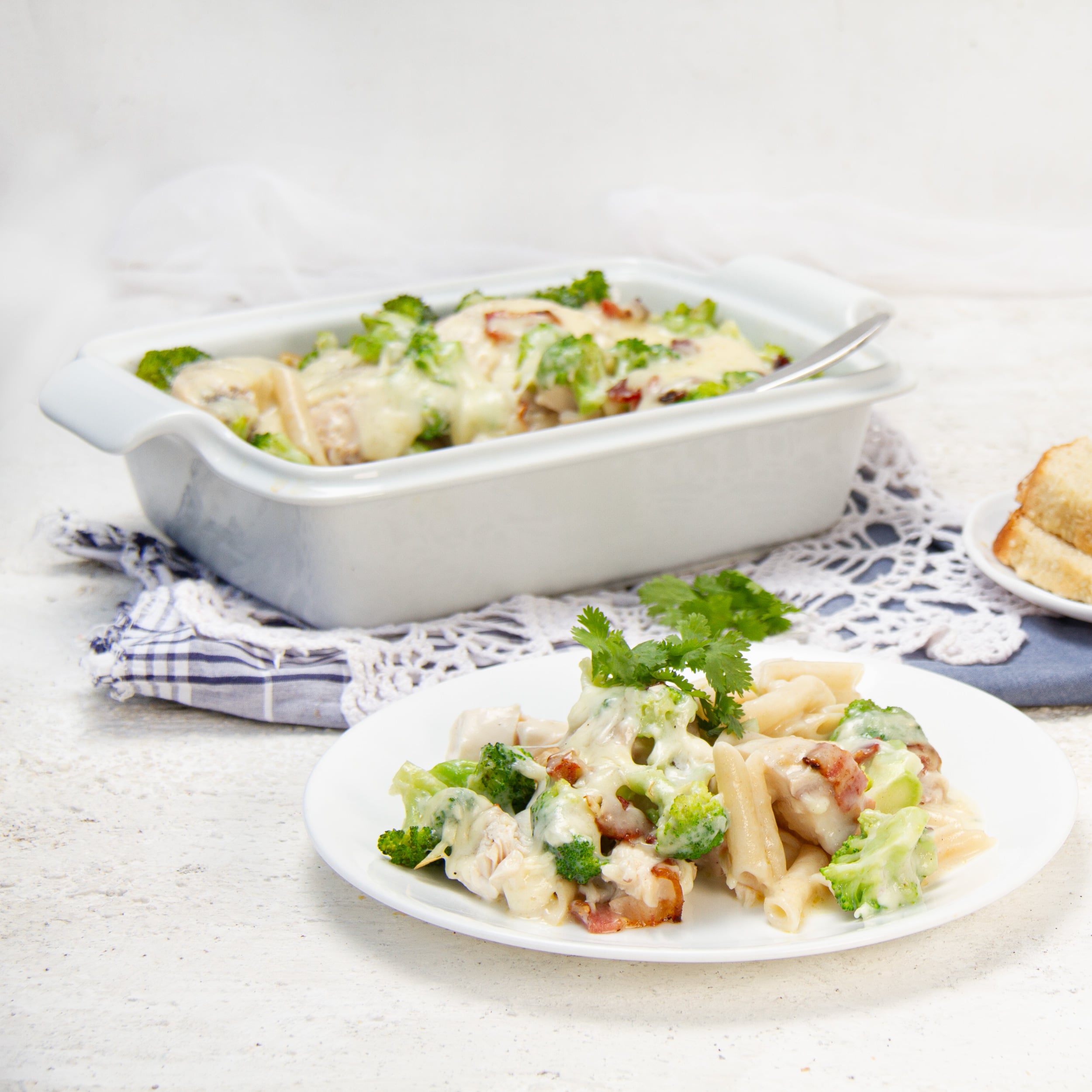 chicken bacon alfredo pasta bake with broccoli and penne served on a white plate in front of the baking dish