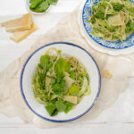 Light and healthy Pesto Pasta on two plates with parmesan and fresh basil on the side.