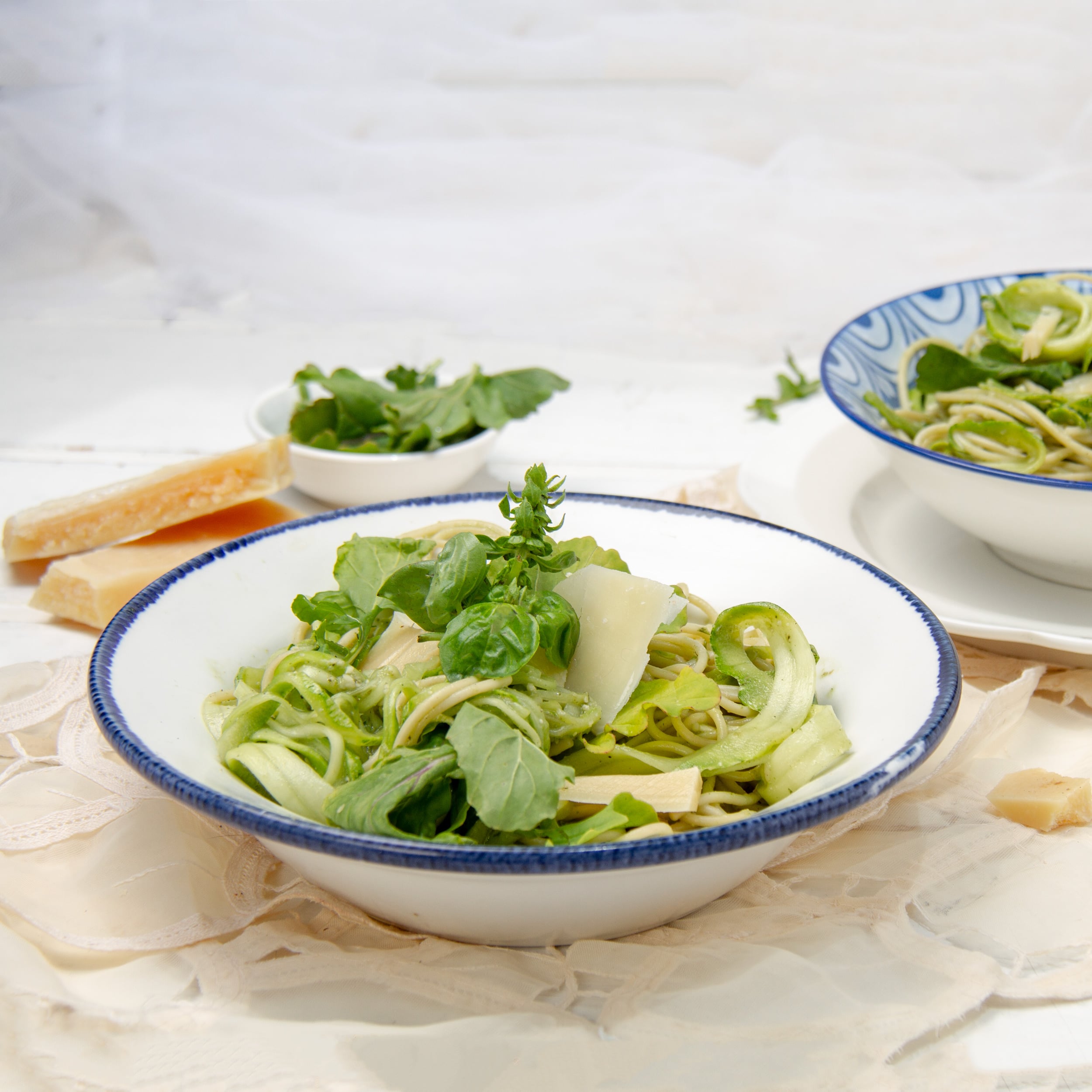 Light and healthy Pesto Pasta on two plates with parmesan and fresh basil on the side.