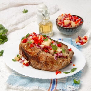 Tropical and delicious pork tenderloin with pineapple salsa on a plate with extra salsa and oil on the side.