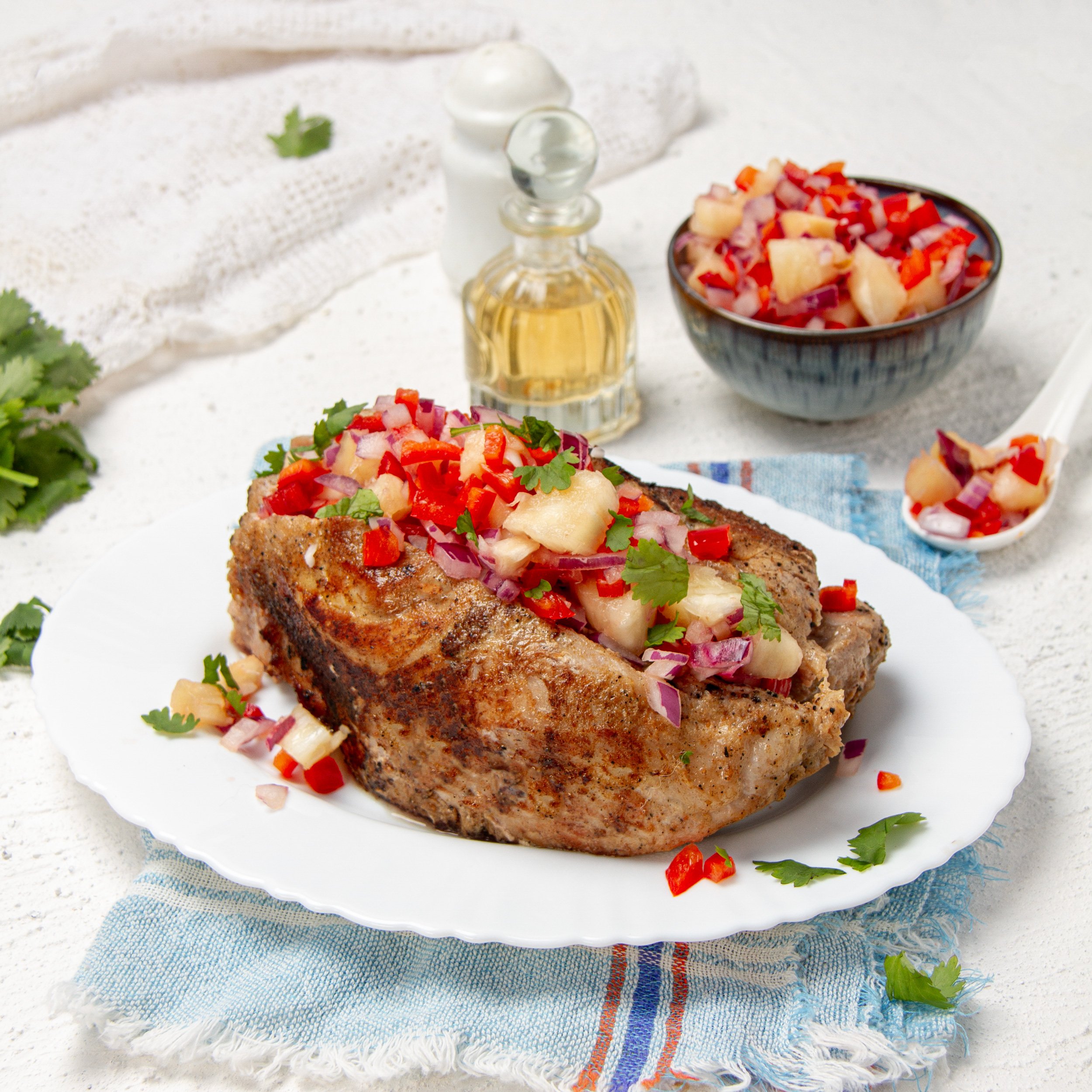 Tropical and delicious pork tenderloin with pineapple salsa on a plate with extra salsa and oil on the side.