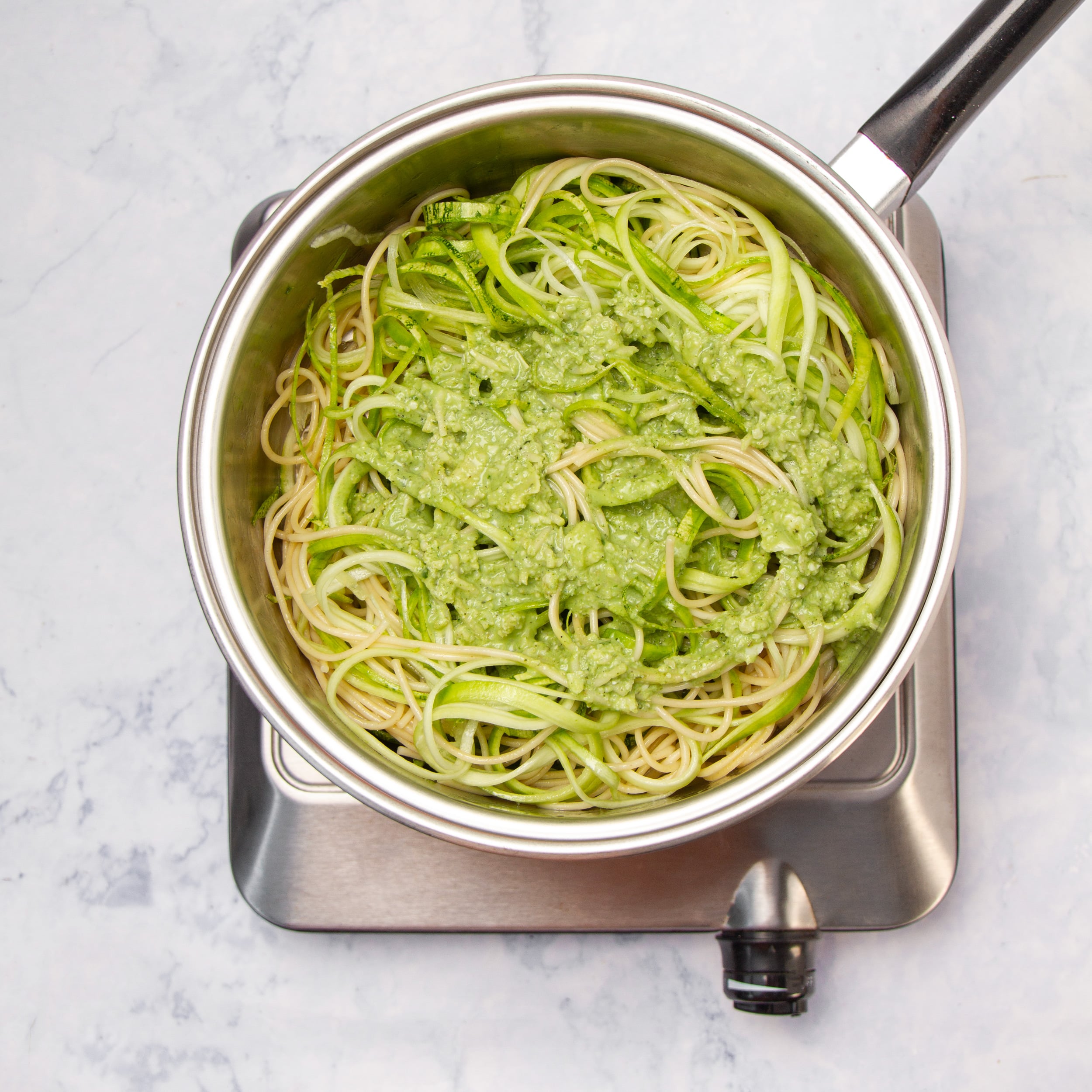Cooked pasta mixed with pesto sauce in a pot.