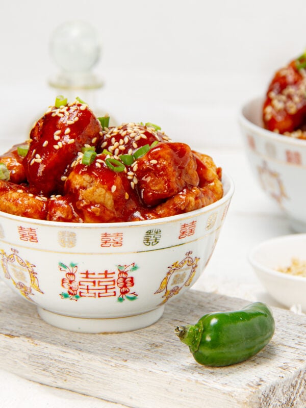 Crispy and bold Firecracker Chicken bites in a bowl with a jalape&ntilde;o on the side.