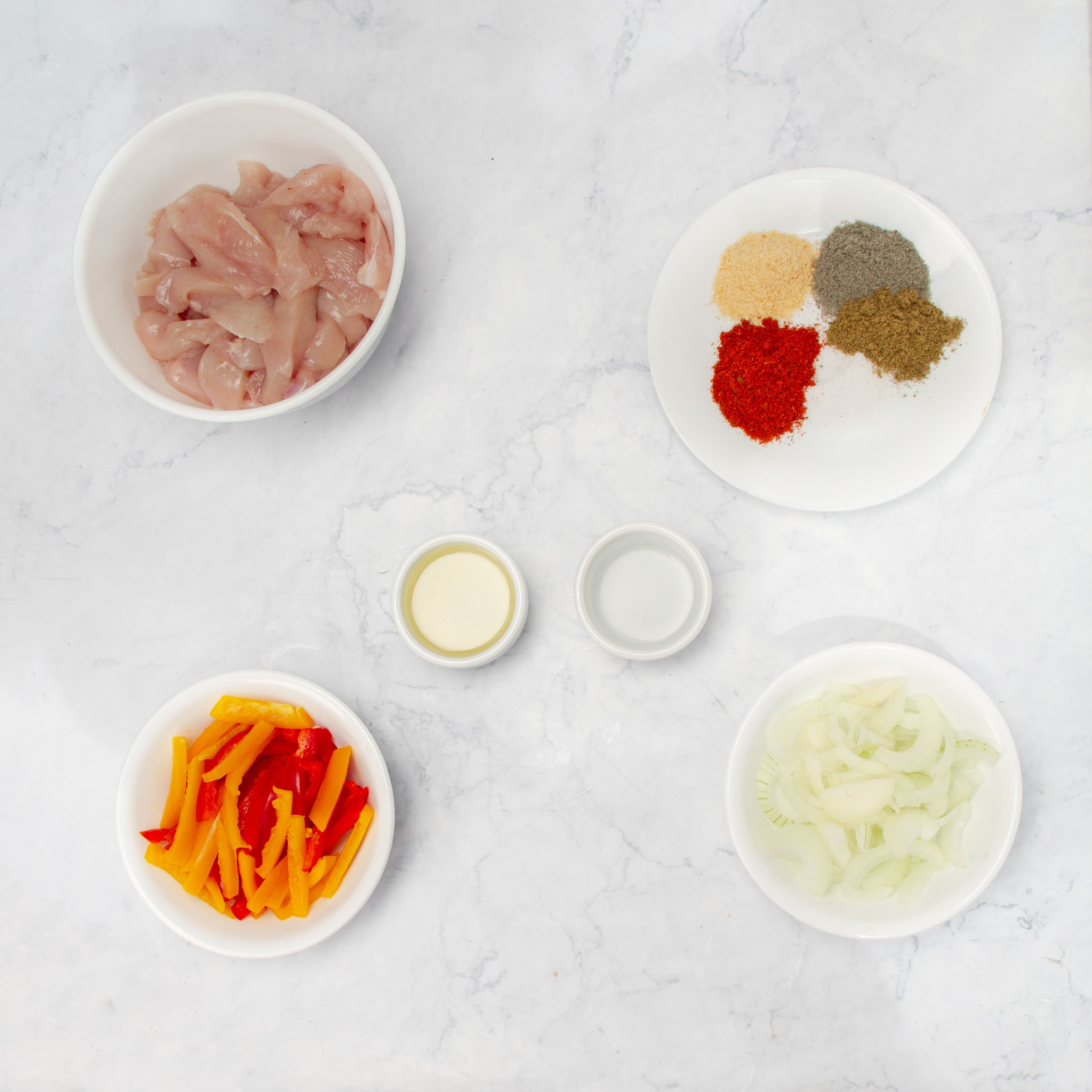 Ingredients for healthy chicken fajitas in separate dishes on a countertop. 