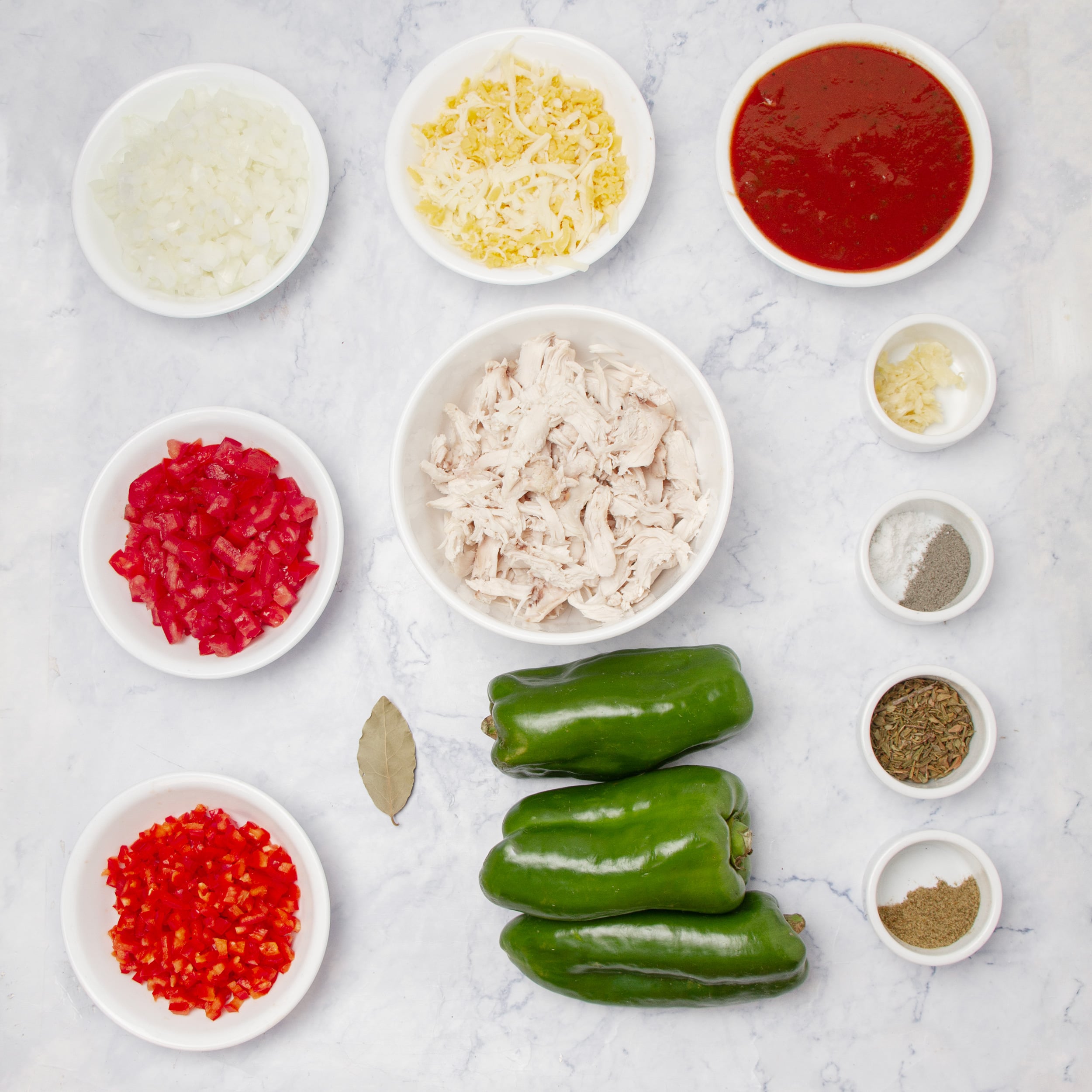 Ingredients for chicken enchilada stuffed poblano peppers: three poblanos, shredded chicken, chopped onion, tomato, red bell pepper, cheese, enchilada sauce, garlic, and spices in small bowls.
