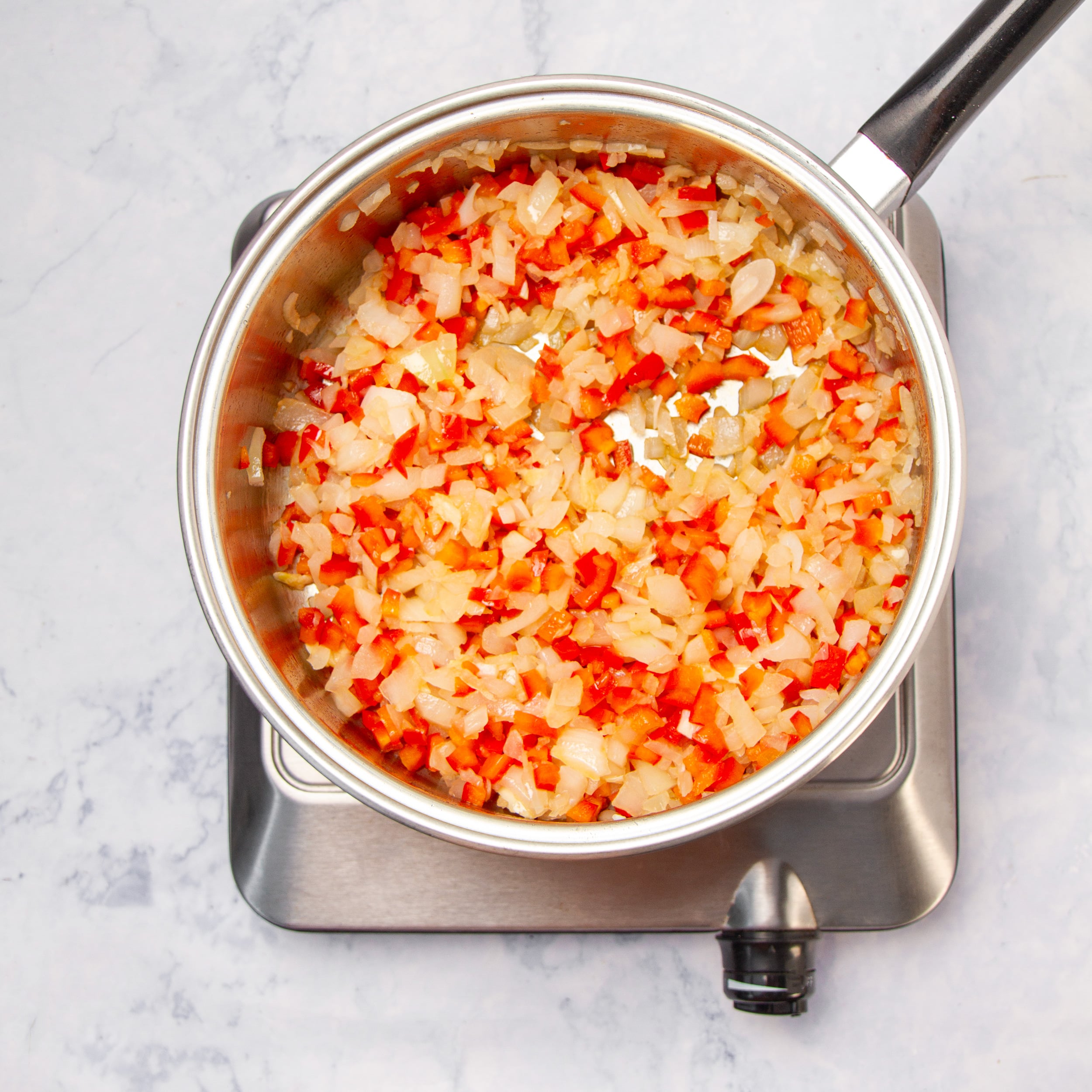 Chopped onion and diced red bell pepper saut&eacute;ing in a saucepan.