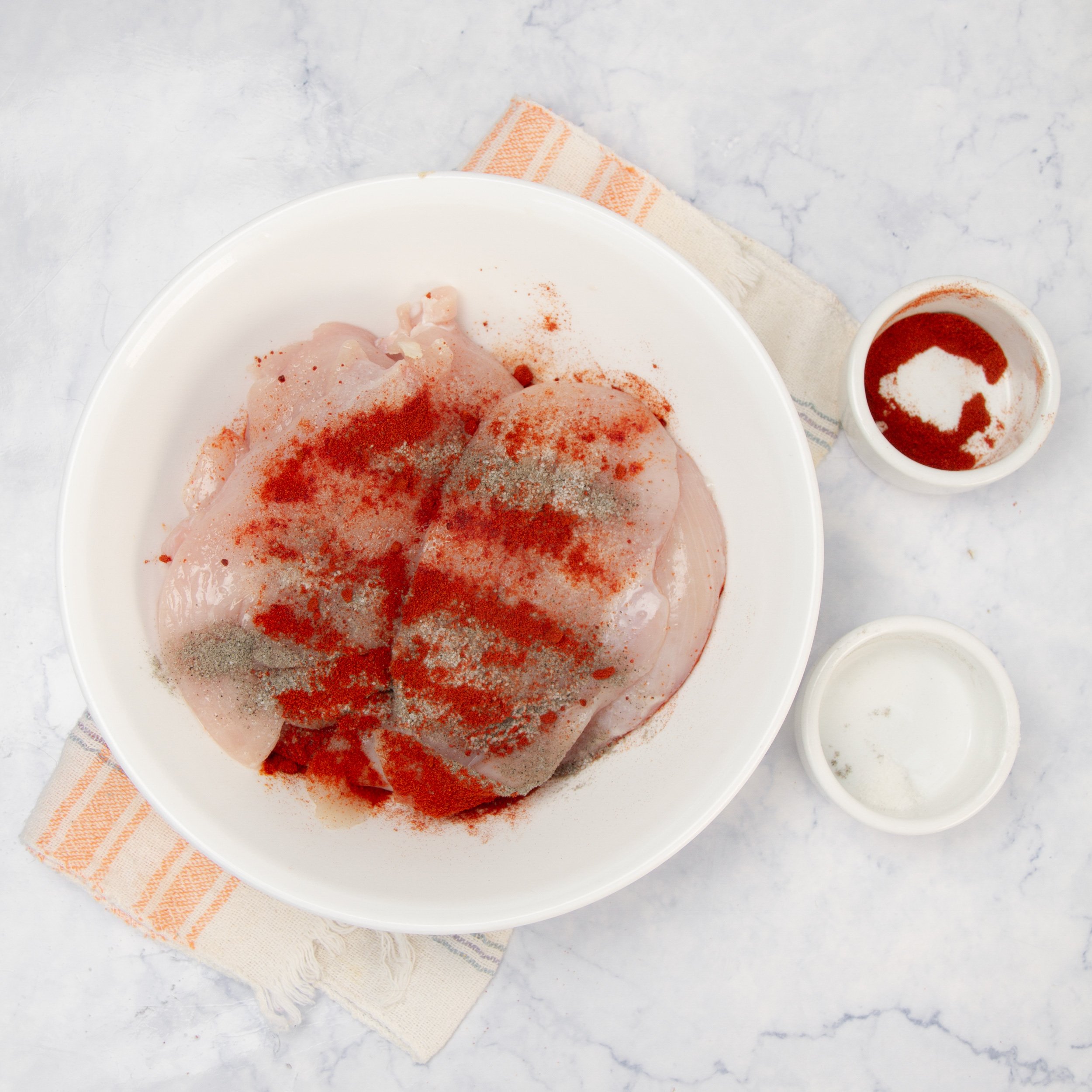 Raw chicken breast with seasoning in a small bowl.