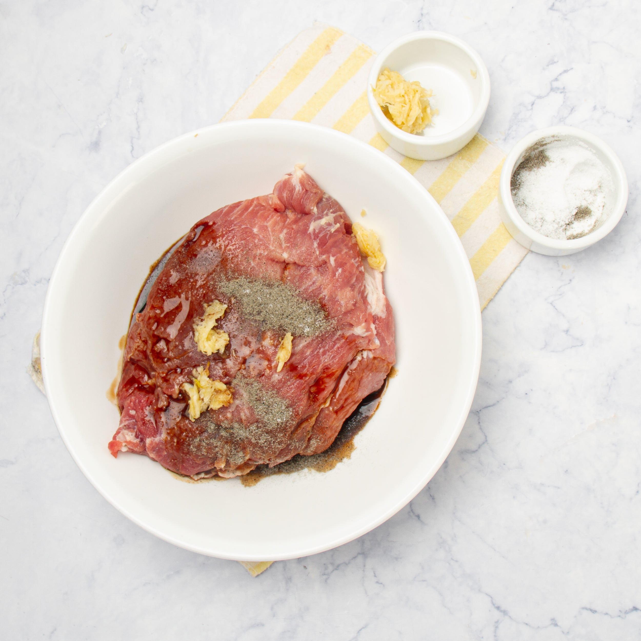 Pork shoulder in a white bowl topped with mashed garlic, salt and liquid smoke.