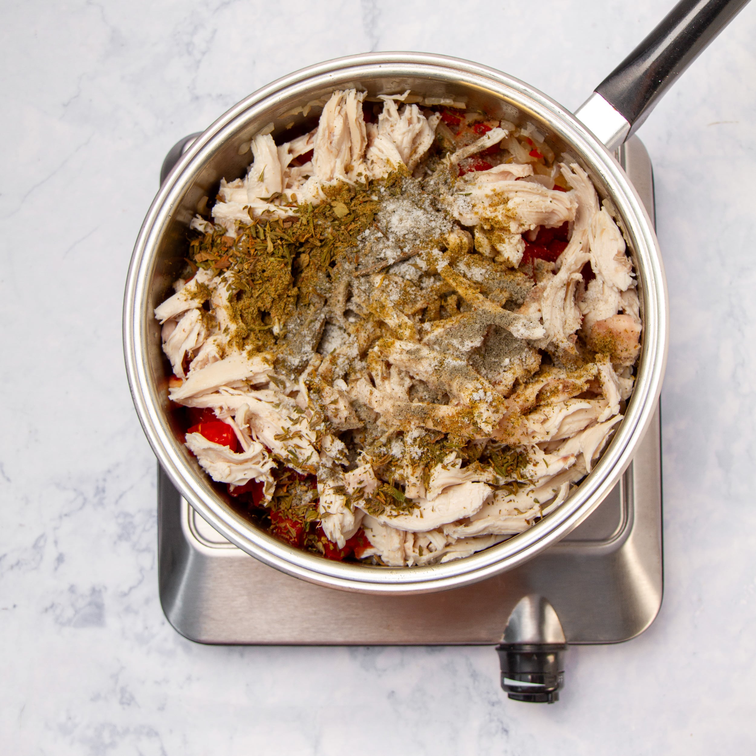 Shredded chicken added to the pan with oregano, cumin, salt, and pepper sprinkled on top.