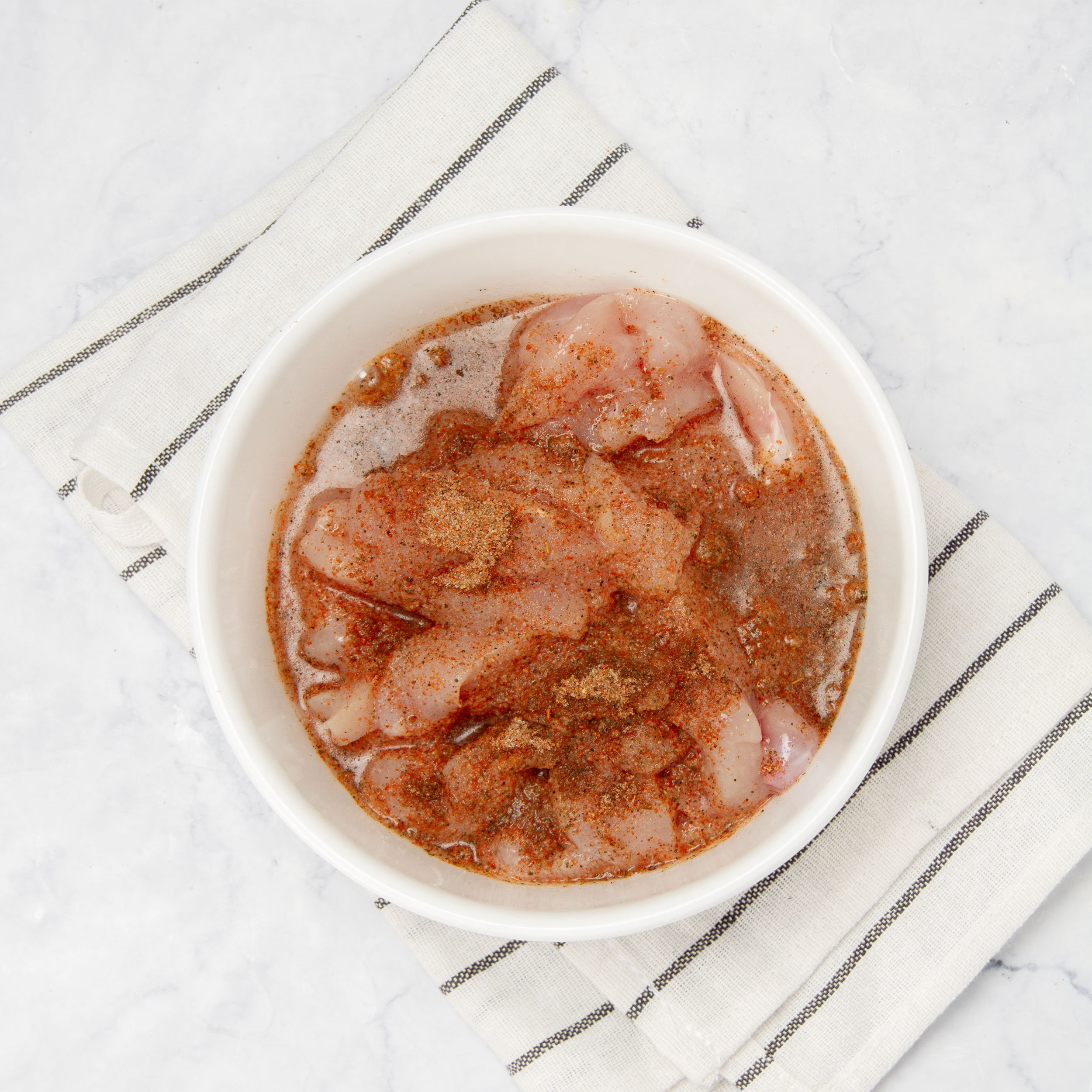 Raw chicken sliced and marinating in fajita spices in a small bowl. 