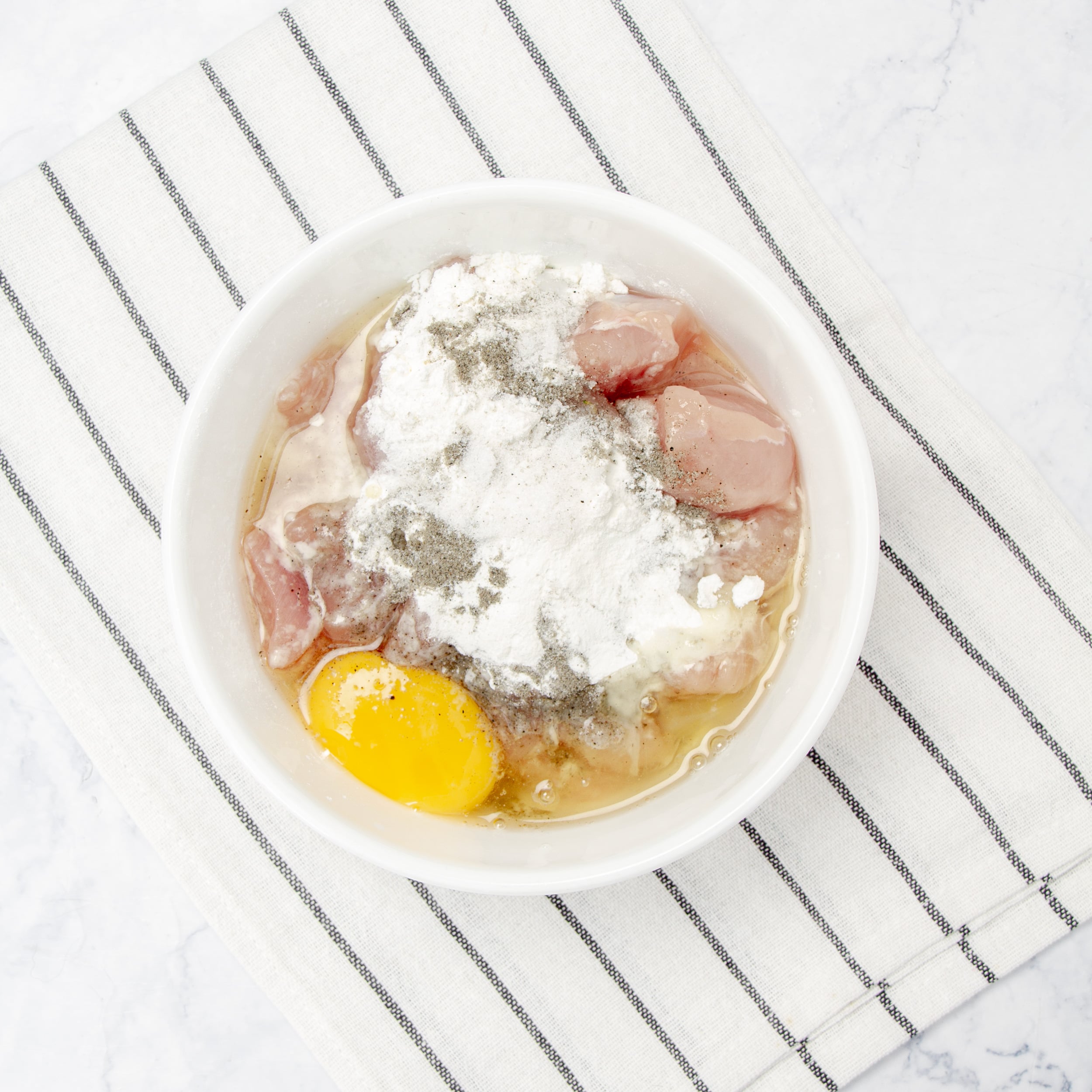 Chicken with flour and eggs in a small bowl.