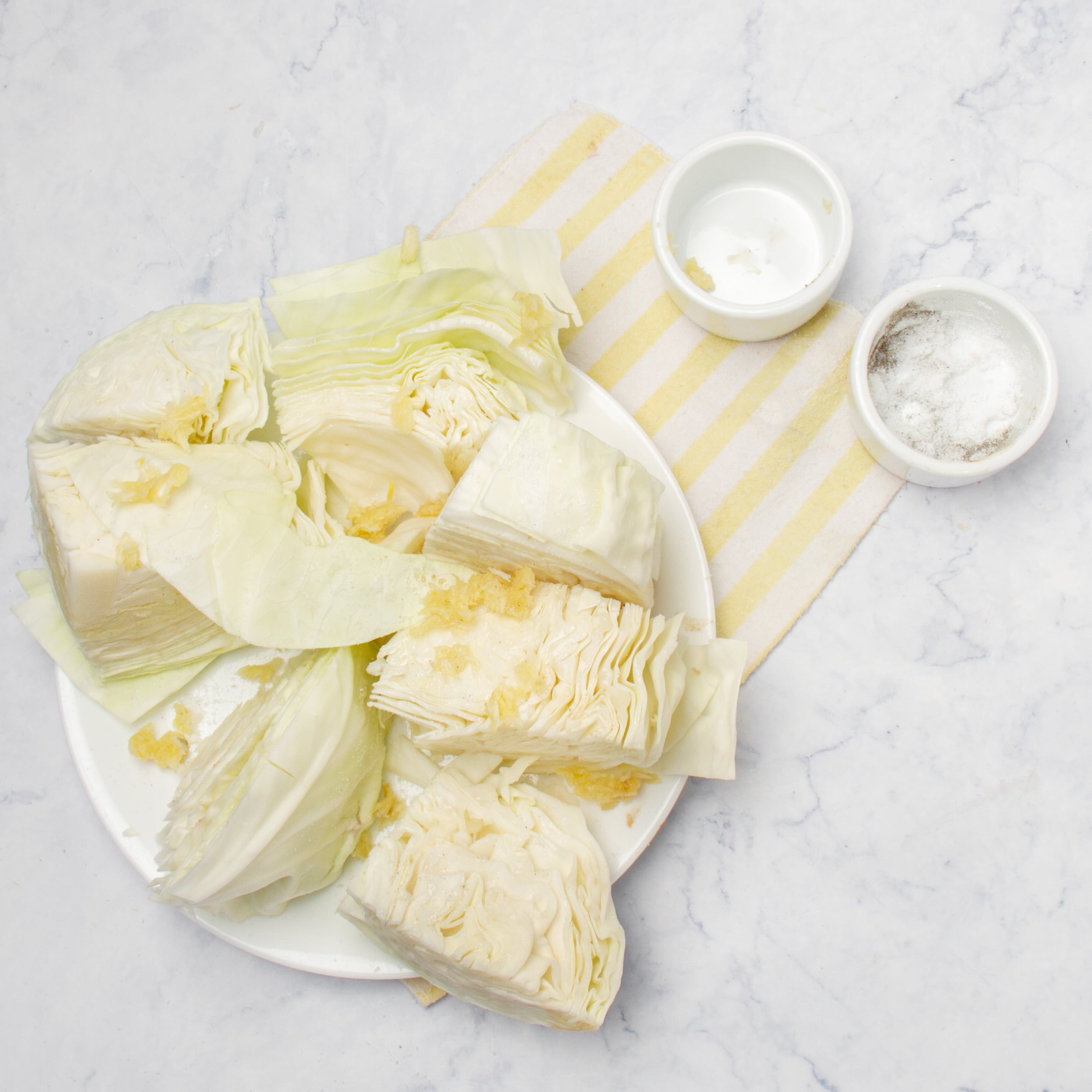 Green cabbage cut into large chunks on a plate with bits of mashed garlic.