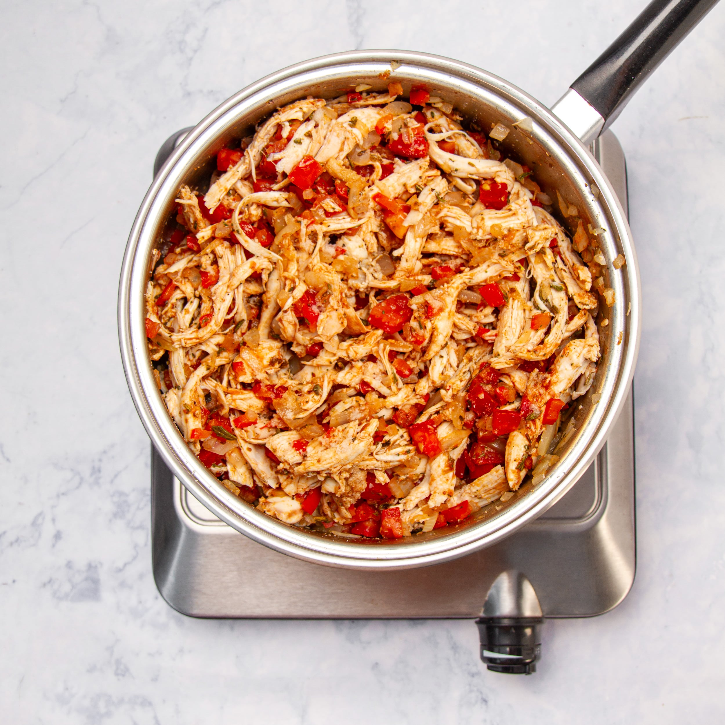 Shredded chicken filling mixed with tomato, onion, red pepper, and enchilada sauce in the pan.
