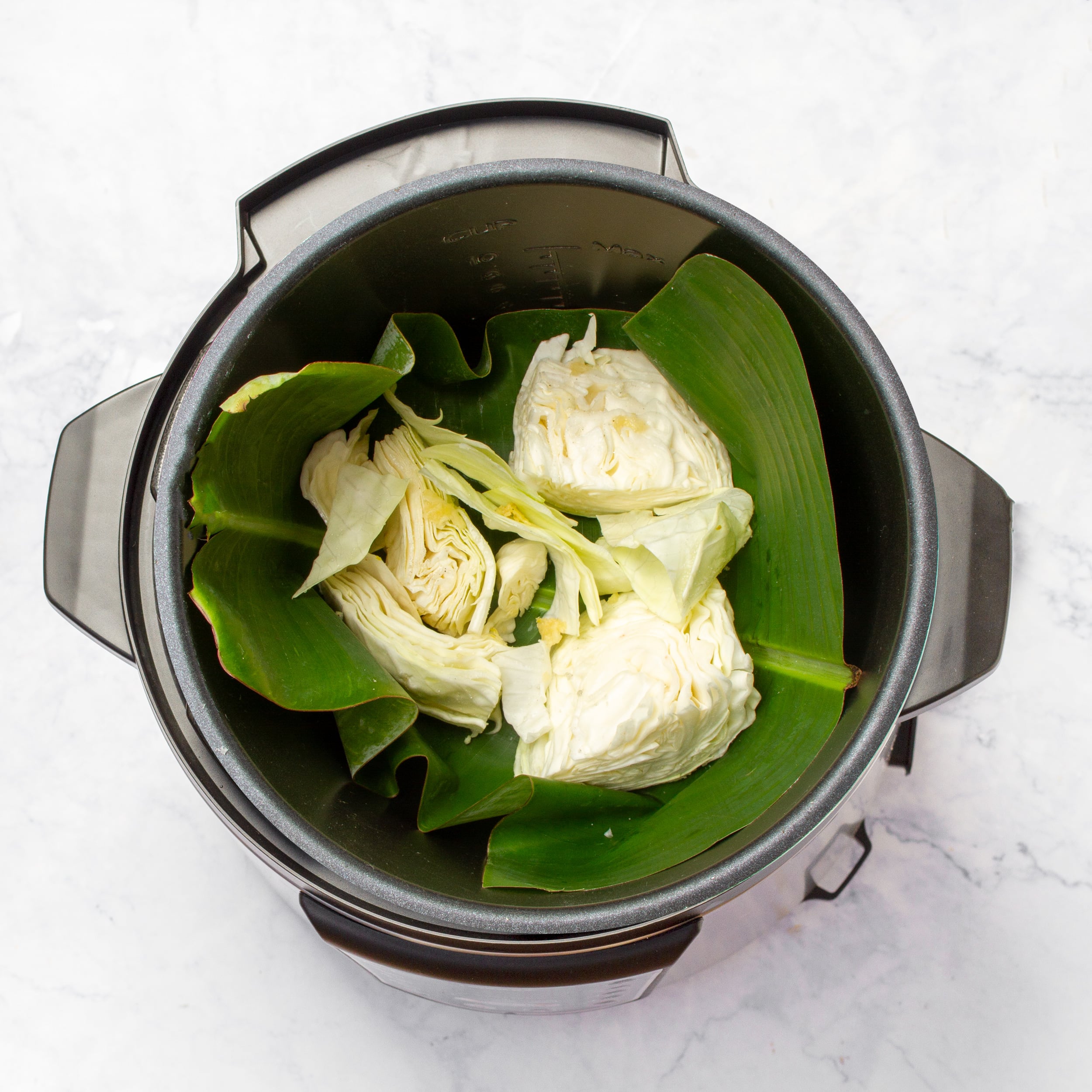 A banana leaf and half of the chopped green cabbage added to the slow cooker pot. 